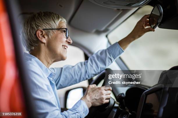 below view of happy senior woman adjusting rear-view mirror in a car. - old woman fixing car stock pictures, royalty-free photos & images