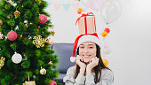 Asian beautiful woman is decorating Christmas tree in white room with gift box placed on the head.Smiling face and happy to celebrate festivel new year holiday.