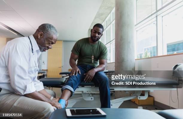 medico ortopedico esamina la caviglia del soldato ferito - caviglia foto e immagini stock