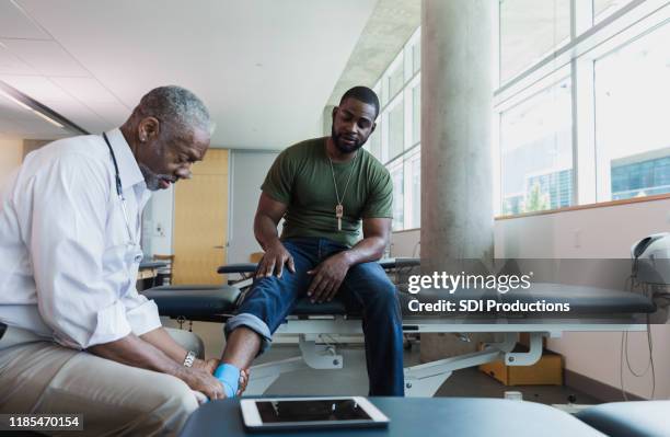 orthopedic doctor examines injured soldier's ankle - injured soldier imagens e fotografias de stock