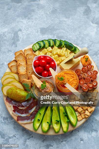 cheese and charcuterie board with cheddar cheese, avocado, duck breast, bacon, cucumber, cherry tomatoes, pear, crispbread, goose pate, hummus with sundried tomatoes, crackers.ideal for party. - charcuterie stockfoto's en -beelden