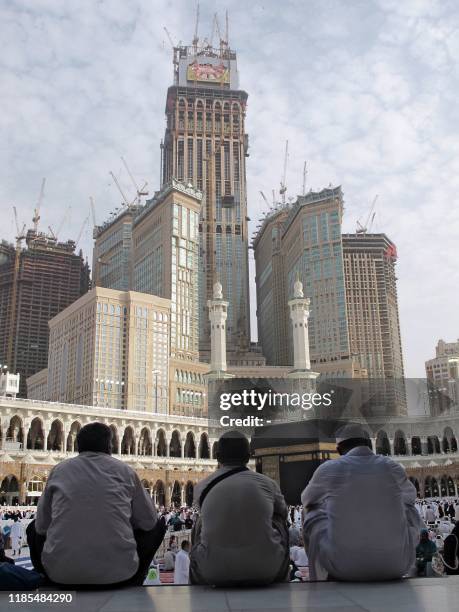 The Mecca Clock Royal Tower hotel is seen under construction topped by the biggest clock in the world with a 45 meters diameter, as Muslims sit in...