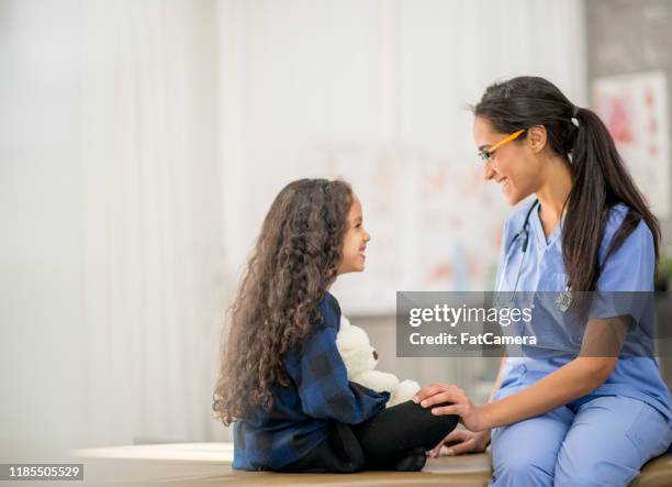 jong meisje zittend cross-legged face to face met verpleegkundige stockfoto - nurse child stockfoto's en -beelden