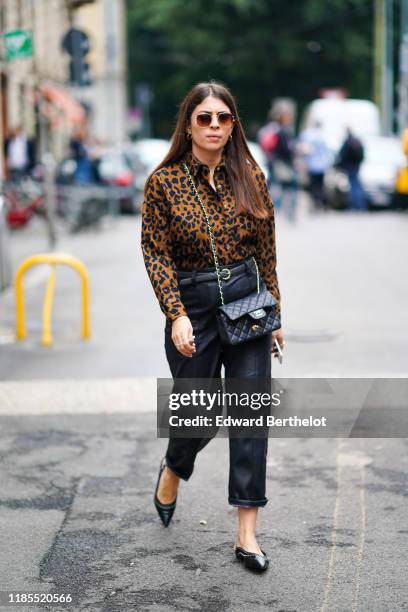 Guest wears sunglasses, a brown and black leopard print shirt, a black belt, black leather rolled up hem crop pants, a black Chanel bag, black...