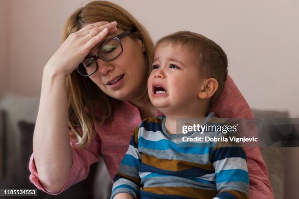 erschöpfte frau hält hand auf dem kopf, wenn sie ein kind hält, das nicht aufhört zu weinen - baby depression stock-fotos und bilder