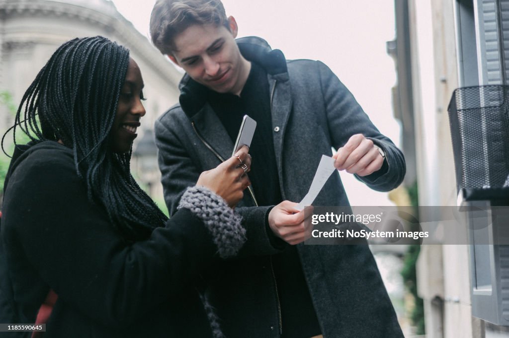 Diverse millennial couple, withdrawing cash at ATM