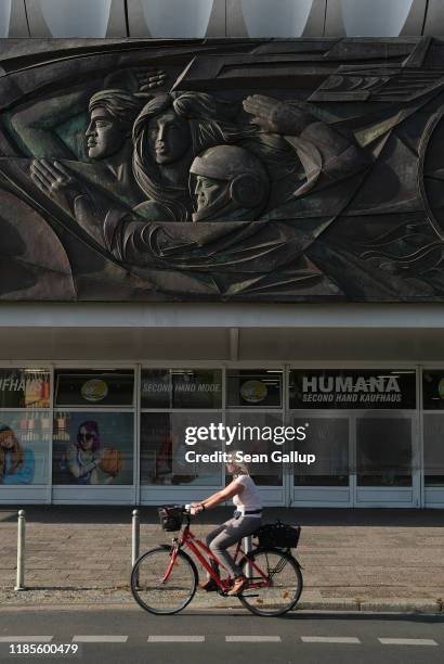Young woman rides a bicycle past a relief that decorates the communist-era "Haus des Reisens" office building at Alexanderplatz on October 14, 2019...