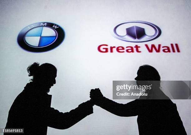 Silhouettes of a man and a woman are seen shaking hands in front of the logos of BMW and Great Wall Motors in Ankara, Turkey on November 30, 2019.