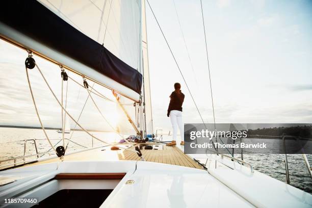 female sailor standing on foredeck of sailboat watching sunset on summer evening - travel experience stock-fotos und bilder