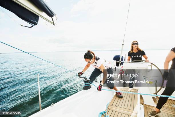 female sailboat crewmember trimming sail with winch during sail on summer evening - sailing team stock-fotos und bilder