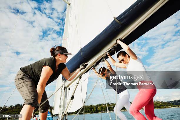 female crew of sailboat pushing on boom during sail on summer afternoon - sail boom stock-fotos und bilder