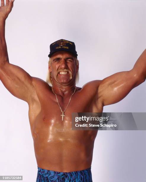 Portrait of American wrestler and actor Hulk Hogan, shirtless, as he raises his arms and clenches his teeth while posing against a white background...