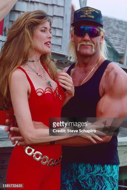 American model and actress Carol Alt, in a red outfit, and wrestler and actor Hulk Hogan, in sunglasses and tank top, pose together on the set of...