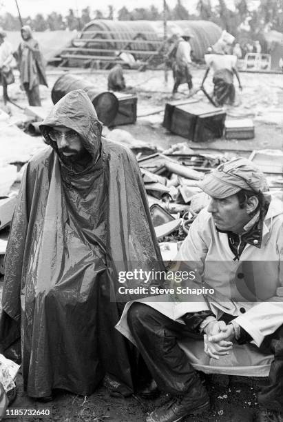 American film director Francis Ford Coppola and an unidentified crew member, both in rain wear, as they sit on the set of their film, 'Apocalypse...