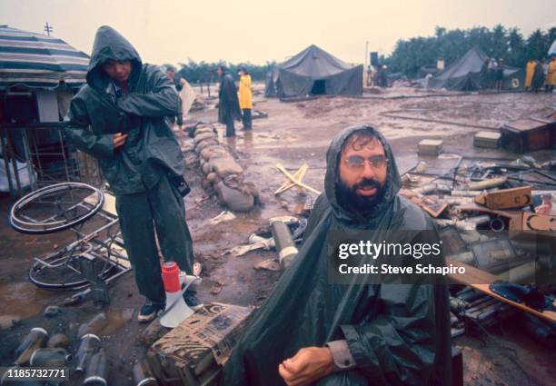 Wrapped in a rain poncho, American film director Francis Ford Coppola sits on the set of his film, 'Apocalypse Now,' Philippines, 1978. The visible...