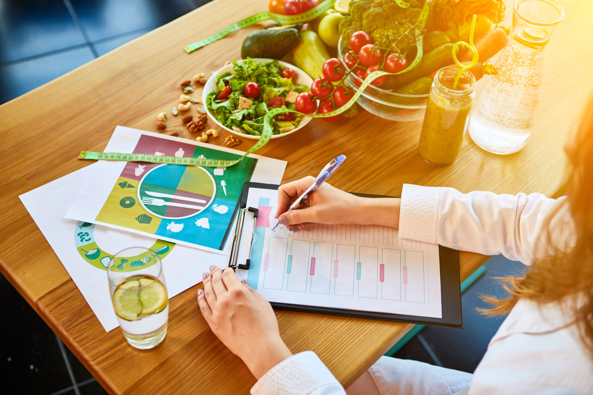 Woman dietitian in medical uniform with tape measure working on a diet plan sitting with different healthy food ingredients in the green office on background. Weight loss and right nutrition concept Woman dietitian in medical uniform with tape measure working on a diet plan sitting with different healthy food ingredients in the green office on background. Weight loss and right nutrition concept