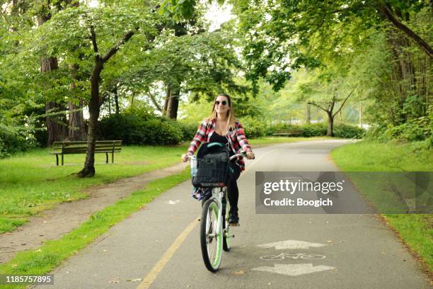 millennial woman on vacation riding a bike on a path in stanley park vancouver canada - bicycle lane stock pictures, royalty-free photos & images
