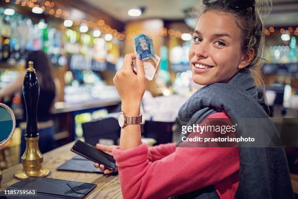 young woman is paying her bill in a bar - british pub stock pictures, royalty-free photos & images