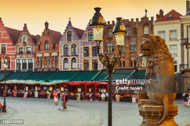traditionele belgische leeuw standbeeld voor het stadhuis en kleurrijke bakstenen gebouwen in market square, brugge, belgië - bruges stockfoto's en -beelden
