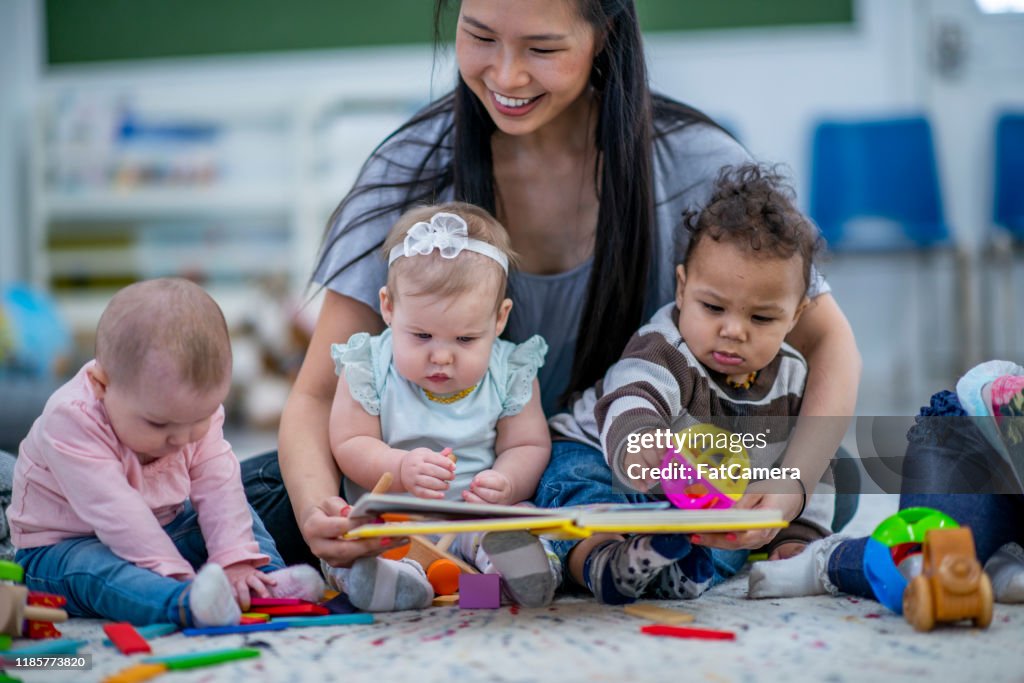 Asilo nido Seduto sul pavimento Lettura ai bambini foto d'archivio