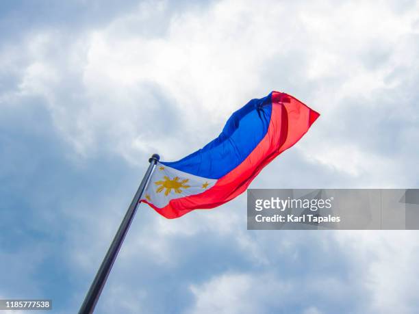a philippine flag on a cloudy sky - philippines national flag stock-fotos und bilder