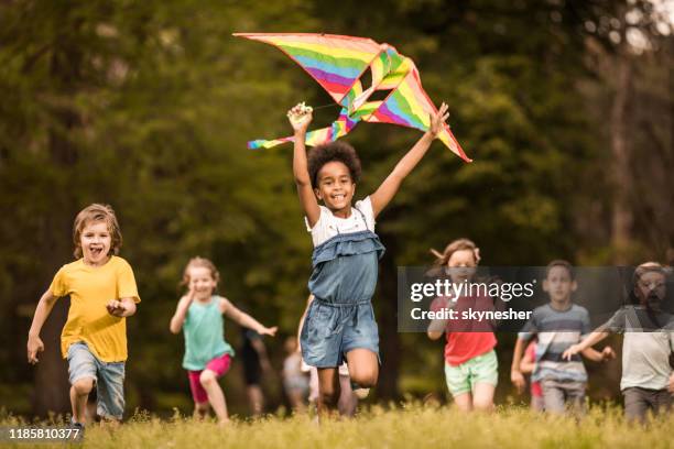 large group of joyful kids running with a kite in springtime. - kite stock pictures, royalty-free photos & images