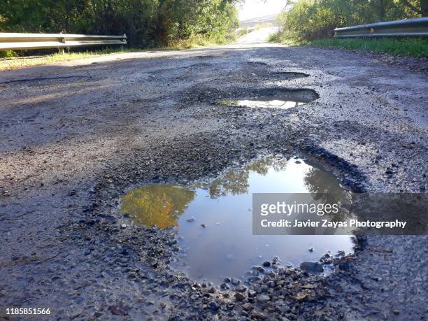 potholes in the middle of a mountain road - pothole stockfoto's en -beelden