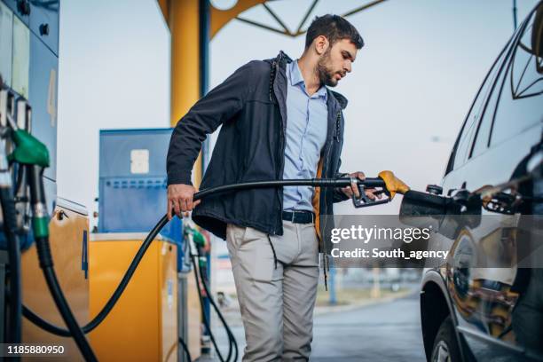 guy pouring fuel in vehicle at the gas station - encher imagens e fotografias de stock