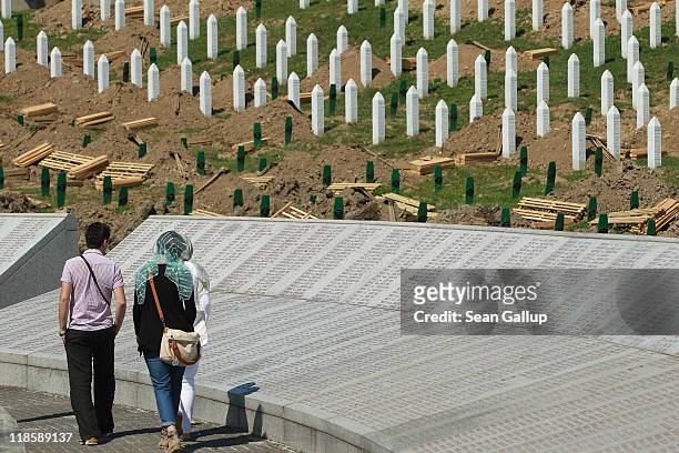 Visitors walk past a headstones and a memorial listing the thousands of victims of the 1995 Srebrenica massacre buried at the Potocari cemetery and...