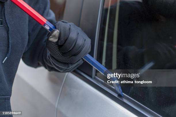 a robber dressed in black holding crowbar at a driver in a car. car thief concept. - hijack imagens e fotografias de stock