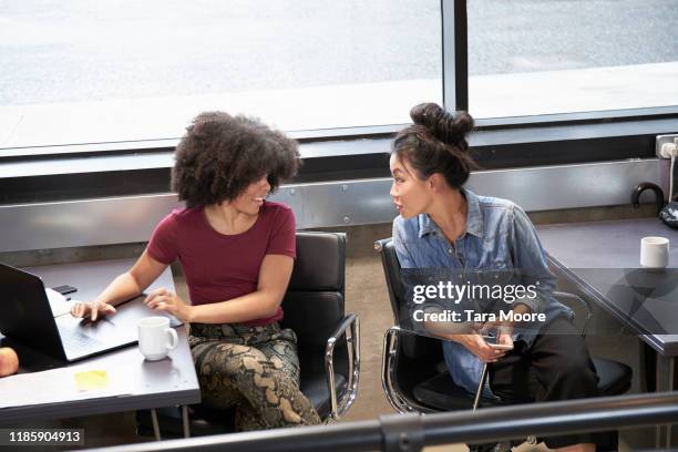 two women sitting at desks working on computers - bavardage photos et images de collection