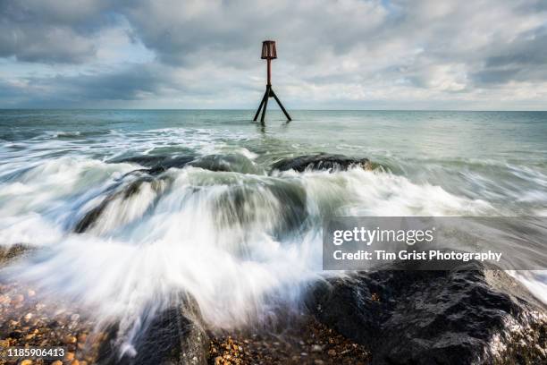 waves crashing  onto rocks and marker post - distance marker stock pictures, royalty-free photos & images