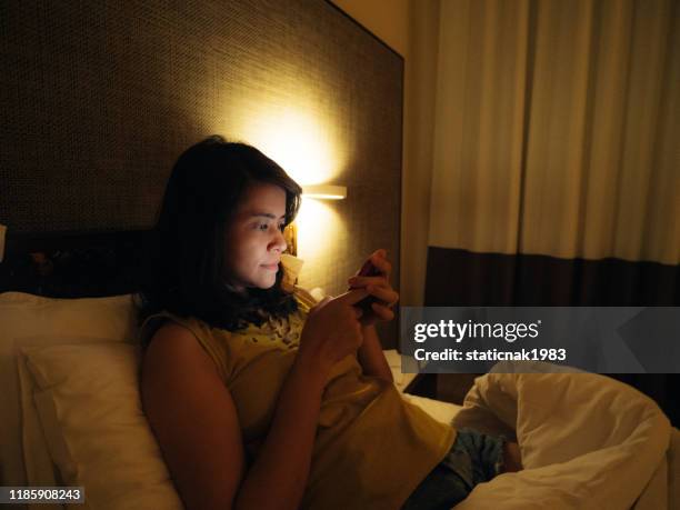 jonge aziatische vrouw gebruik mobiele telefoon in de slaapkamer - donkere kamer stockfoto's en -beelden