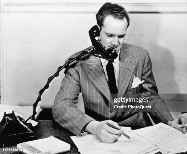 An unidentified man demonstrates the 'Exex-Arm,' a hands-free device for holding a telephone, Milwaukee, Wisconsin, late 1930s or early 1940s. The...