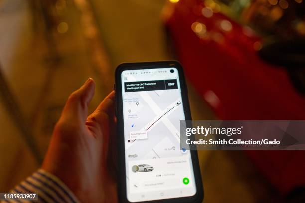 Close-up of hand of a man holding a mobile phone on a city street at night and using the Uber app to hail an Uber ridesharing vehicle, Los Angeles,...