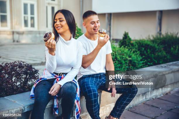 happy couple eat donuts and smiling. - biting donut stock pictures, royalty-free photos & images