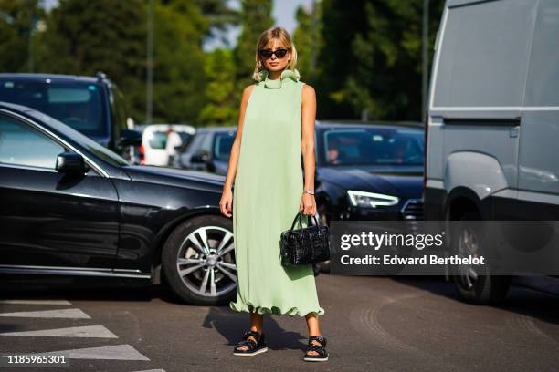 Xenia Adonts wears sunglasses, a high neck green dress, a black leather bag, black shoes, outside the Tod's show during Milan Fashion Week...