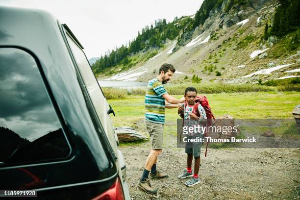 Father helping son adjust backpack before beginning camping trip