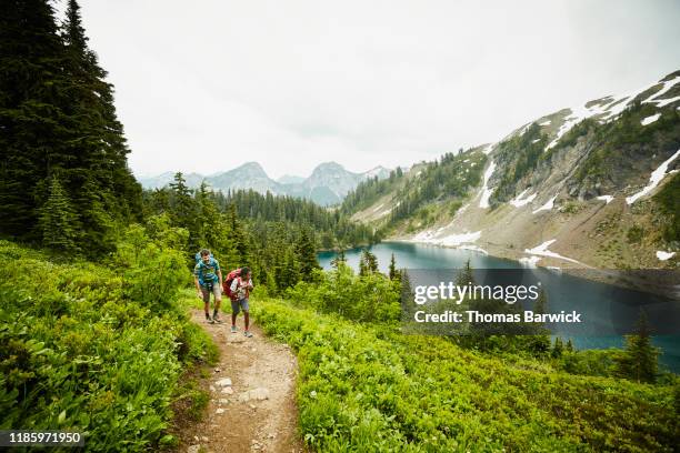 father and son hiking on mountain trail above alpine lake - tough love stock-fotos und bilder
