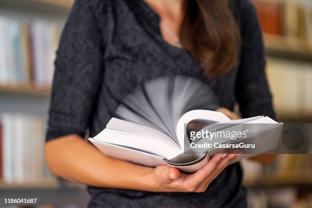 donna adulta che sfoglia le pagine di un libro in biblioteca - sfogliare libro foto e immagini stock