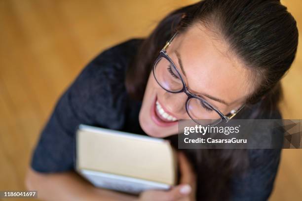 high angle view of smiling young woman carrying a thick book - thick reading glasses stock pictures, royalty-free photos & images