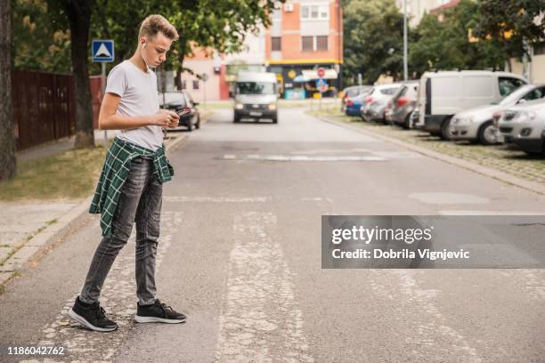 kind überquert die straße an einem fußgängerüberweg und hört musik auf seinem handy - crosswalk stock-fotos und bilder