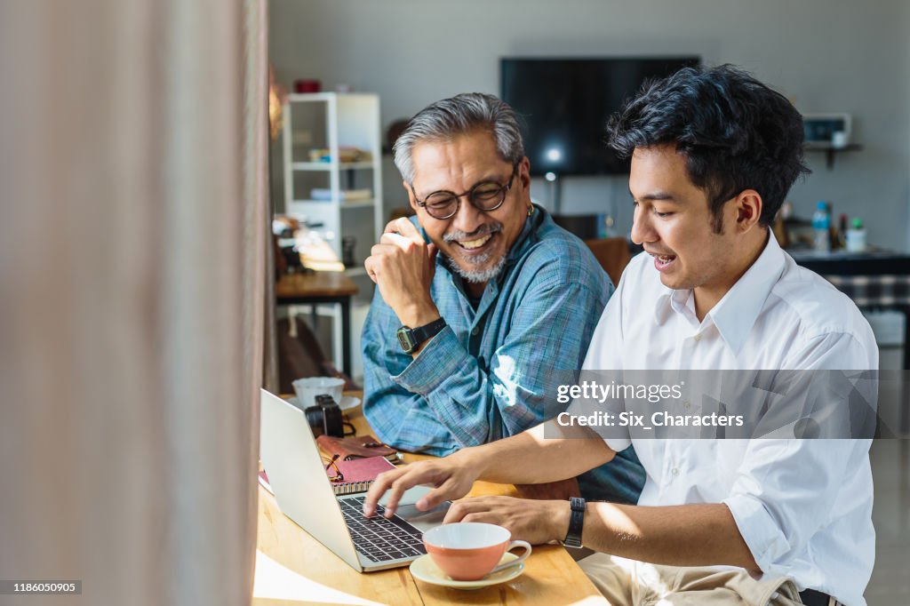 Aziatische Senior vader en zijn volwassen zoon het gebruik van laptop computer terwijl zittend thuis