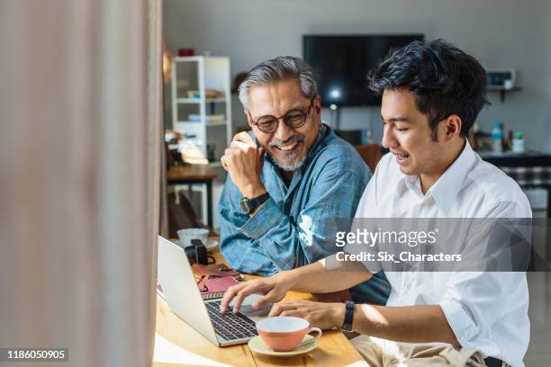 asiatiska senior far och hans vuxna son använder bärbar dator när du sitter hemma - vuxet barn bildbanksfoton och bilder