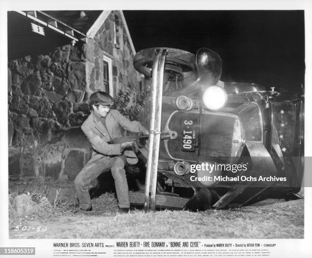 Michael J Pollard with a machine gun near an overturned car in a scene from the film 'Bonnie and Clyde', 1967.