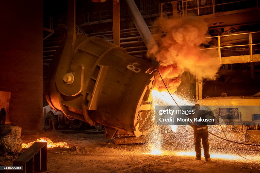 Steelworker cleaning pouring end of flask during steel pour in steelworks