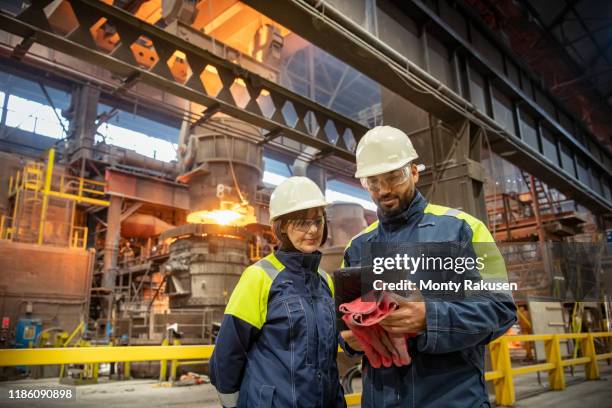 male and female steelworkers using digital tablet during steel pour in steelworks - steel industry stock pictures, royalty-free photos & images