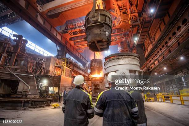 three steelworkers watching molten steel pour in steelworks - fonderie photos et images de collection