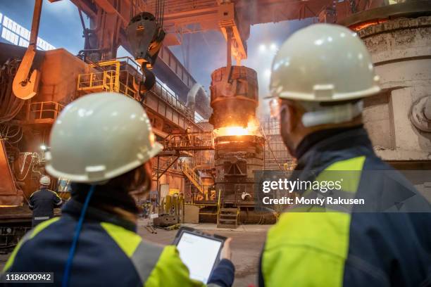 male and female steelworkers using digital tablet during steel pour in steelworks - metal industry stock-fotos und bilder