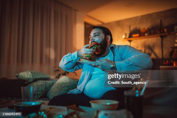 uomo che guarda una partita sportiva e mangia hamburger - rimpinzarsi foto e immagini stock
